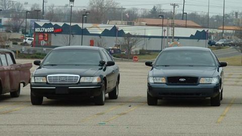 1998 Ford Crown Victoria - Two Ford Crown Victorias are parked side-by-side in a parking lot with a building in the background.