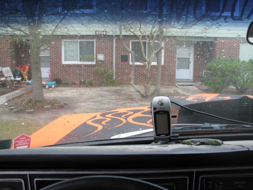 Windshield view over an orange hood with black flames and a Garmin eTrex GPS on the glass
