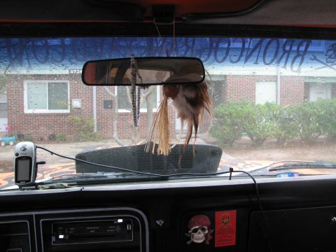 1979 Ford Bronco - Interior view over a black dash and slider-style heater control panel, looking out a rainy windshield lettered "BRONCORACING.COM" with a sk…
