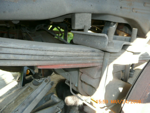 Close-up of a vehicle's leaf spring suspension with a jack underneath
