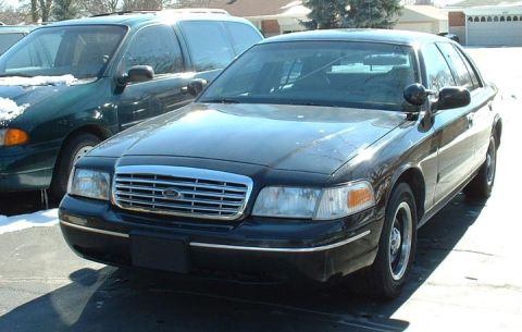 1998 Ford Crown Victoria - Front view of a 1998 Ford Crown Victoria parked outdoors with a minivan beside it.