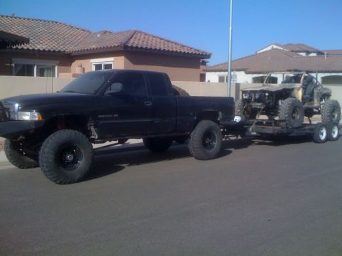 1966 Ford Bronco - A black pickup truck tows a custom off-road vehicle on a trailer under a clear sky.