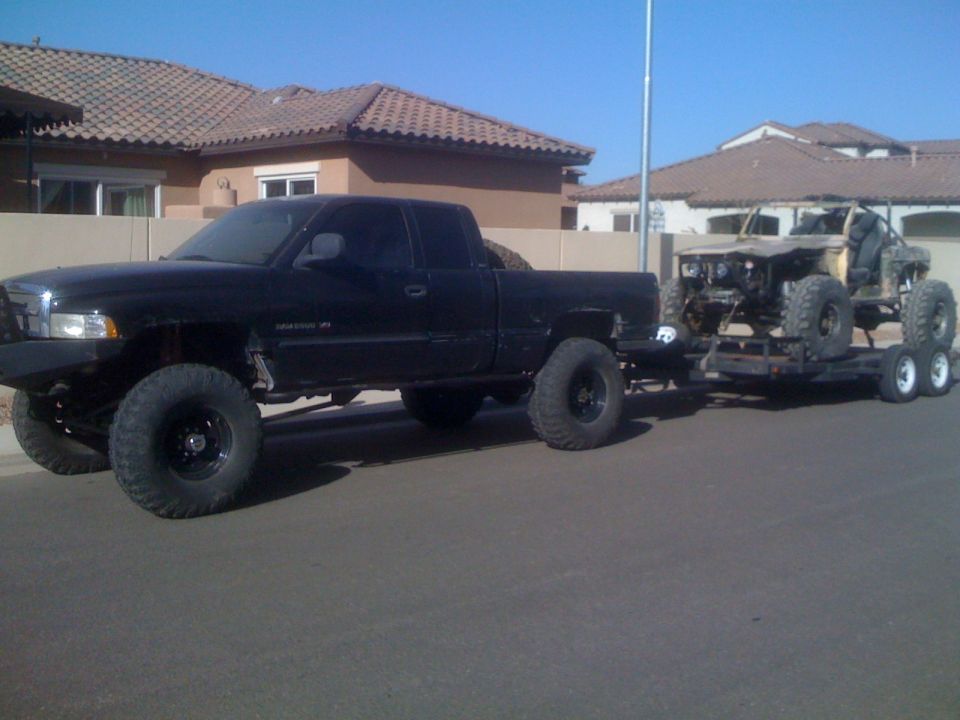 Black pickup truck with large tires towing a custom off-road vehicle on a trailer