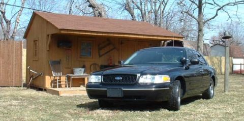 1998 Ford Crown Victoria - A black 1998 Ford Crown Victoria is parked in front of a wooden shed on a sunny day.