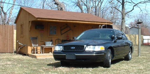 Black 1998 Ford Crown Victoria parked in front of a wooden shed