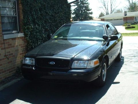 1998 Ford Crown Victoria - A black 1998 Ford Crown Victoria is parked in front of a brick building on a sunny day.