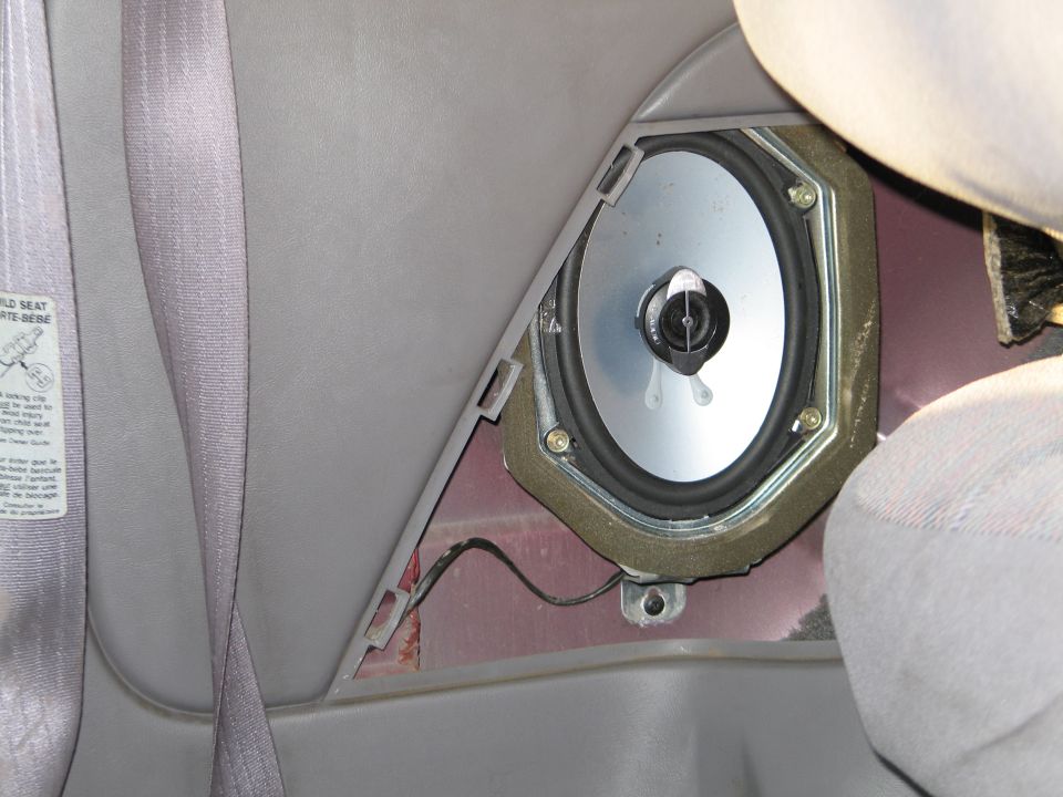 Interior view of a car's rear speaker mounted in the door panel, with a seatbelt visible