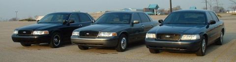 1998 Ford Crown Victoria - Three Ford Crown Victoria sedans are parked side-by-side in an outdoor lot under a hazy sky.