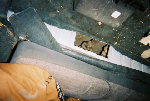 1991 Ford Bronco - Damage to the interior floor panel reveals exposed metal and wiring beneath the carpet.