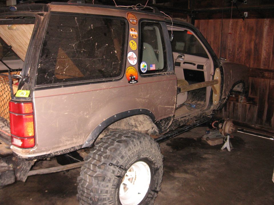 Brown SUV with large off-road tires, missing driver's door, and front wheel removed