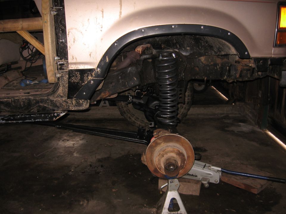 Rear suspension and wheel assembly of a vehicle on jack stands, with "SUPERMOTORS" visible