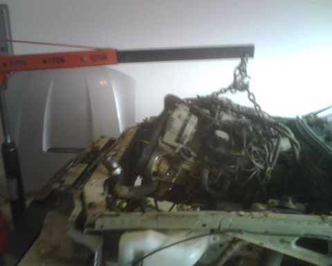 1999 Ford Mustang - An engine is suspended by chains and an engine hoist, being removed from a vehicle's engine bay.