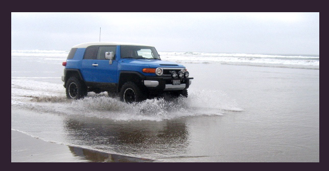 Blue 2007 Toyota FJ Cruiser driving through shallow water on a beach