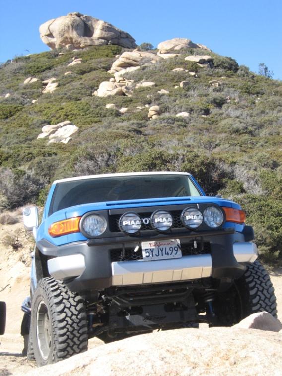 Blue 2007 Toyota FJ Cruiser with PIAA lights and large off-road tires on a rocky trail
