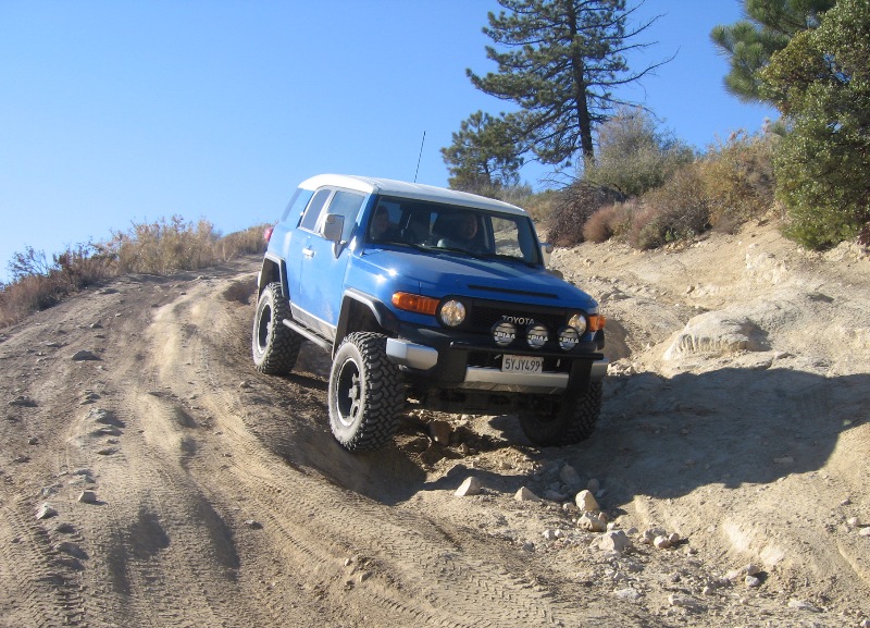 Blue 2007 Toyota FJ Cruiser climbing a steep dirt trail with aftermarket lights