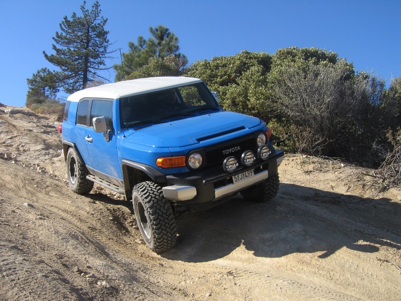 Blue 2007 Toyota FJ Cruiser driving on a dirt trail with trees and blue sky