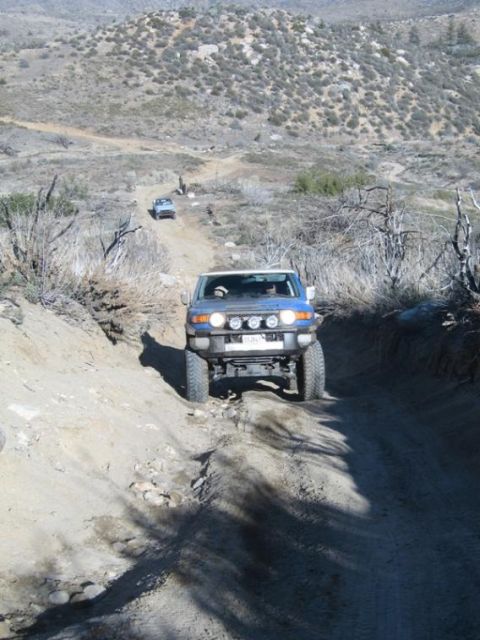 2007 Toyota FJ Cruiser - Two off-road vehicles navigate a dusty, mountainous trail under a clear sky.