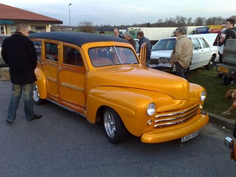 1991 Ford Crown Victoria - This vintage woody wagon is parked at an outdoor event with other vehicles and people around.
