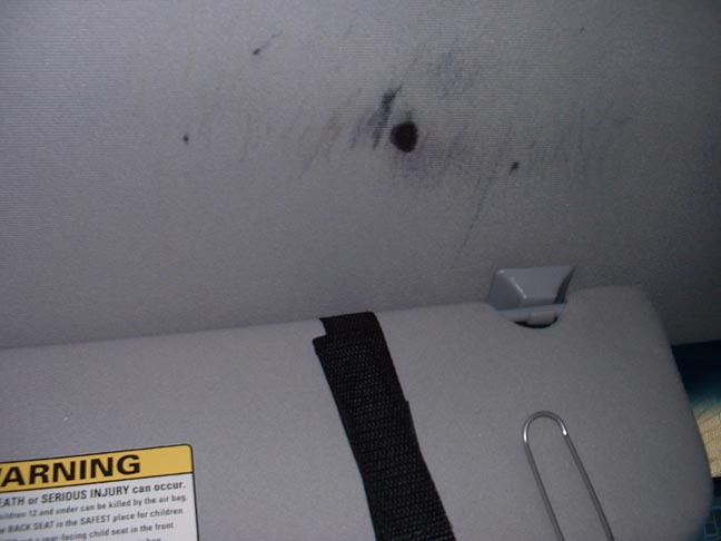 Car ceiling with some dark marks and a sun visor. Warning label visible on visor