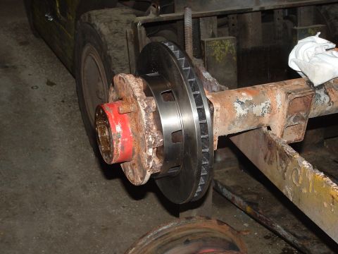 1979 Ford Bronco - Close-up of a vehicle axle with a brake rotor and hub, with a forklift in the background.