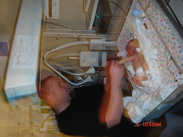 Father looking at his newborn baby in an incubator in a hospital room