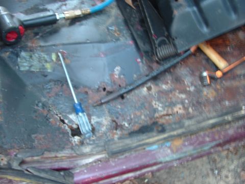 1979 Ford Bronco - The interior of a vehicle shows significant rust and damage, with tools scattered on the floor.