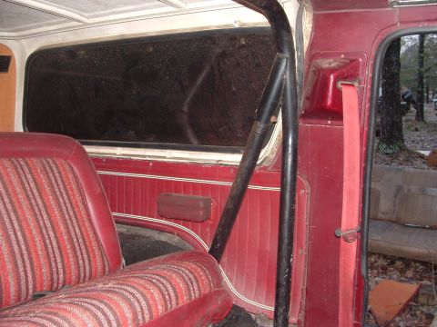 1979 Ford Bronco - The interior of an older vehicle shows red striped seats and a roll bar, with a red seatbelt attached.