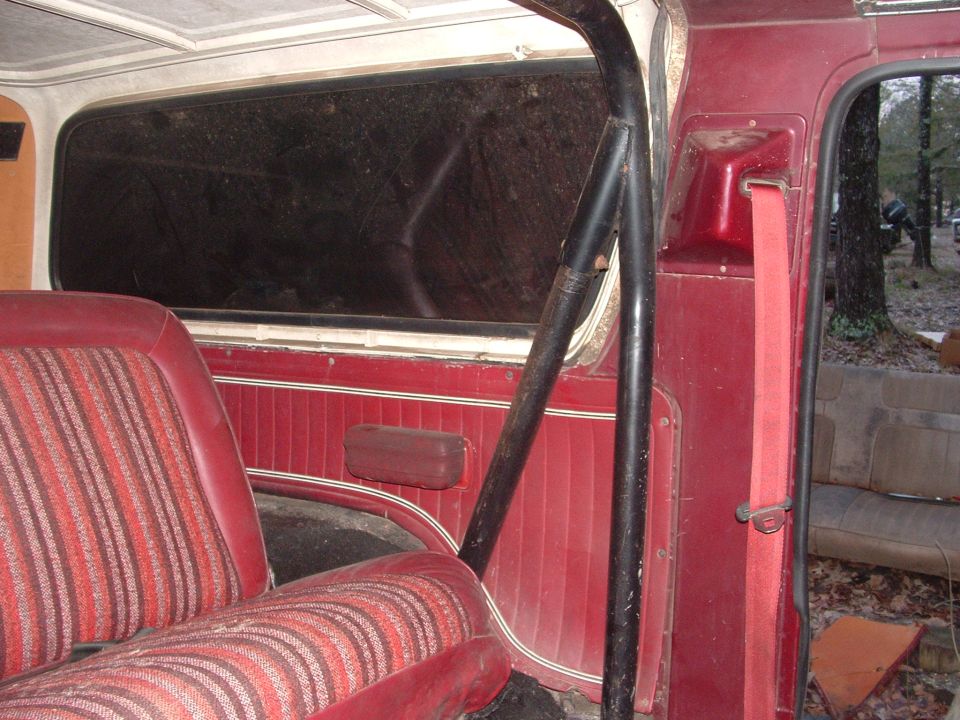Red striped seats and red door panel inside a vehicle with a black roll bar. A red seatbelt is visible