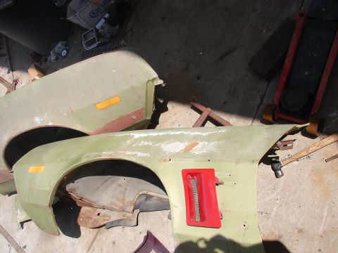 1973 Ford Ranchero - Two pale lime-green front fenders lie face-up on a concrete garage floor, each with an amber front side-marker lamp and one still carrying…
