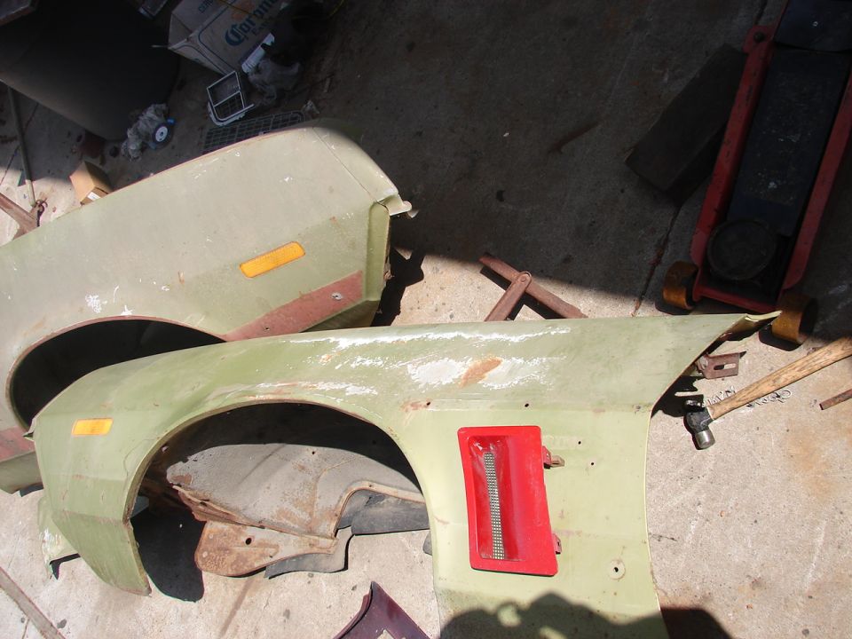 Two lime-green car front fenders with amber markers and red side vent lying on a garage floor