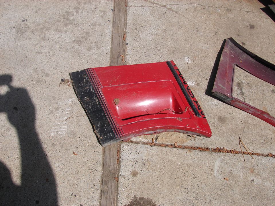 Red hood scoop panel with black stripes lying on a concrete driveway
