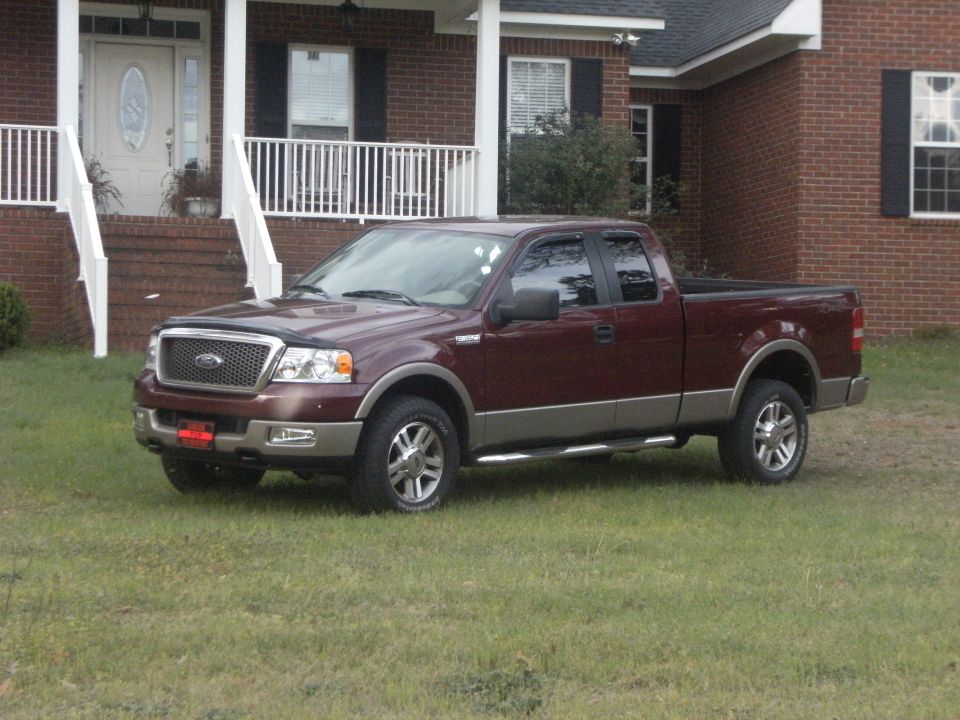 2005 Ford F-150 pickup truck, maroon with tan lower body trim, parked on grass in front of a brick house