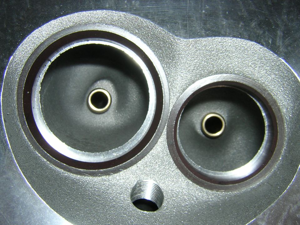 Close-up of an engine cylinder head with two valve ports and a threaded hole