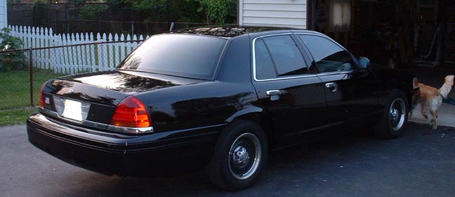 Black 1998 Ford Crown Victoria parked outside, dog near garage