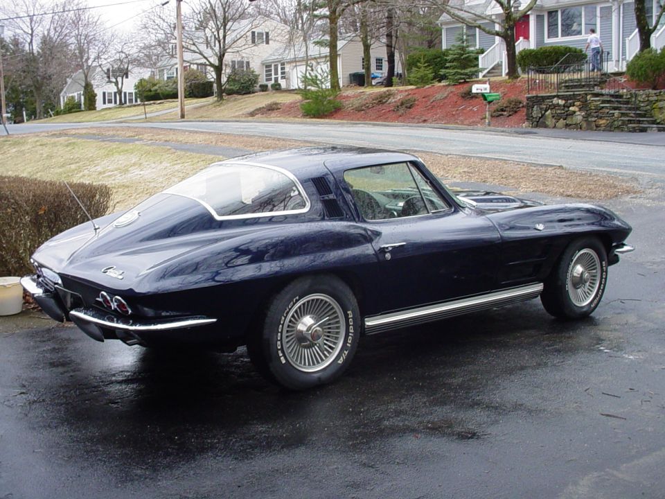 Dark blue coupe parked on wet asphalt, houses in background