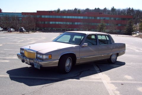2001 Ford Crown Victoria - This Cadillac sedan is parked in a lot with a large brick building behind it.