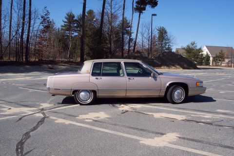 2001 Ford Crown Victoria - Side view of a tan 1993 Cadillac sedan parked in an asphalt lot with trees and houses in the background.