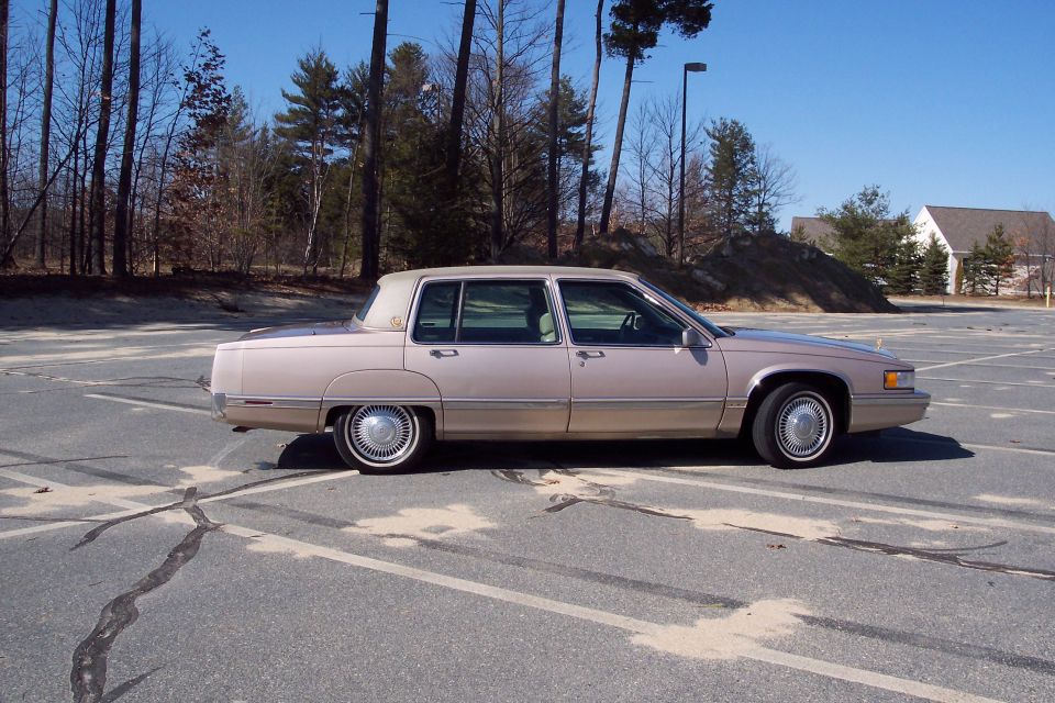 Tan 1993 Cadillac sedan, side view. Parked in an empty lot