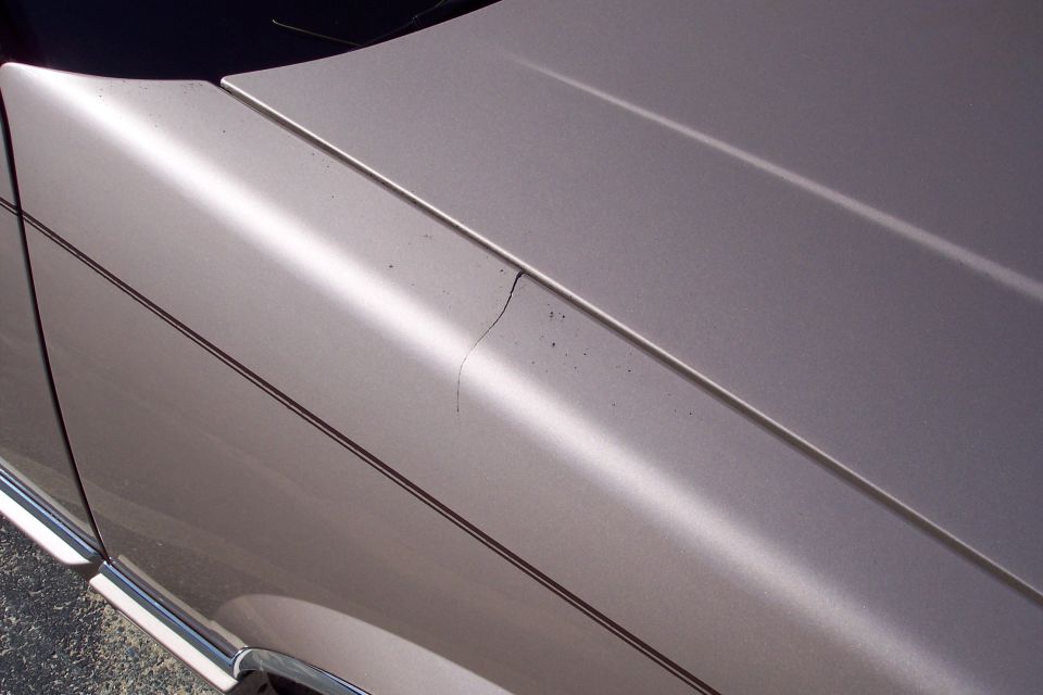 Tan car hood and fender with a dark pinstripe and a crack on the fender