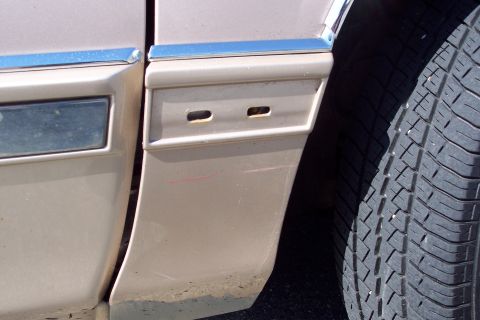 2001 Ford Crown Victoria - Close-up of a tan car's side panel, showing chrome trim, a tire, and two rectangular openings on the lower section.