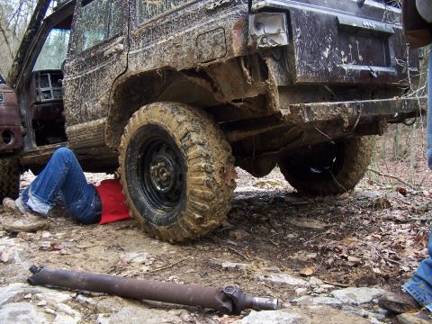 2002 Ford Sport Trac - Person working on a muddy Jeep Cherokee XJ off-road, with a driveshaft removed.