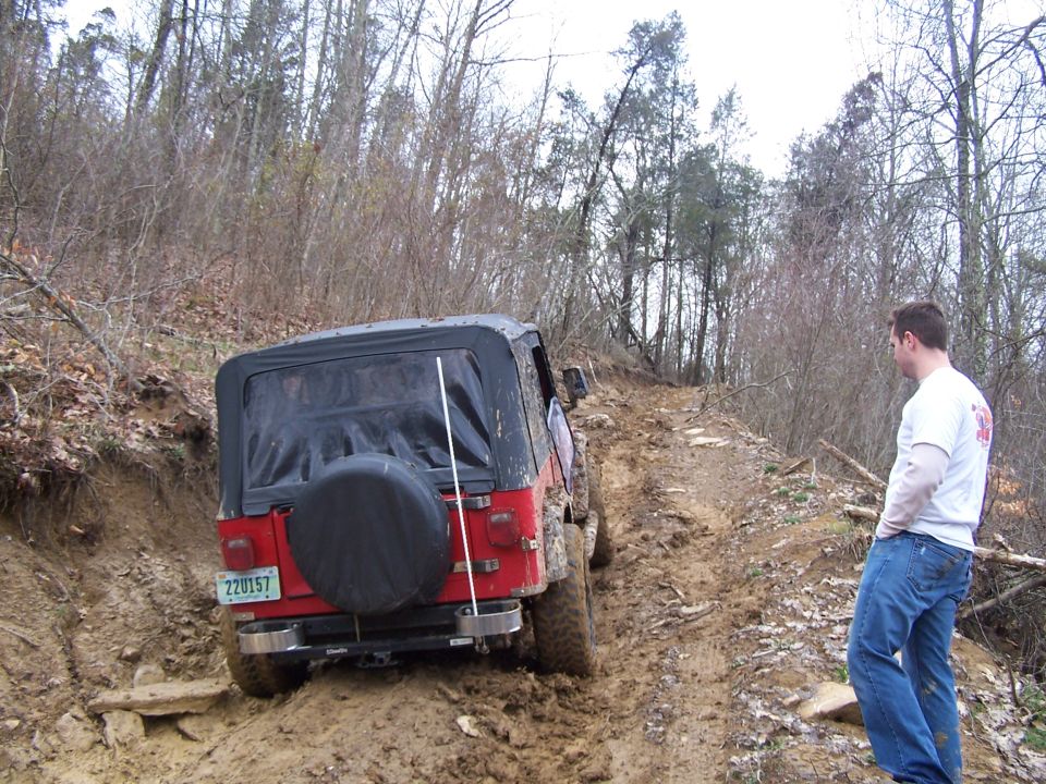Red Jeep Wrangler on a muddy offroad trail, rear view, spare tire visible