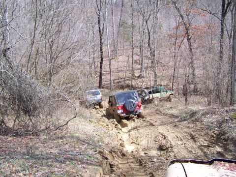 2002 Ford Sport Trac - Multiple off-road vehicles struggle on a challenging muddy track in a wooded area.