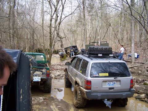 2002 Ford Sport Trac - Off-roading adventure in a muddy forest with multiple vehicles navigating the challenging terrain.