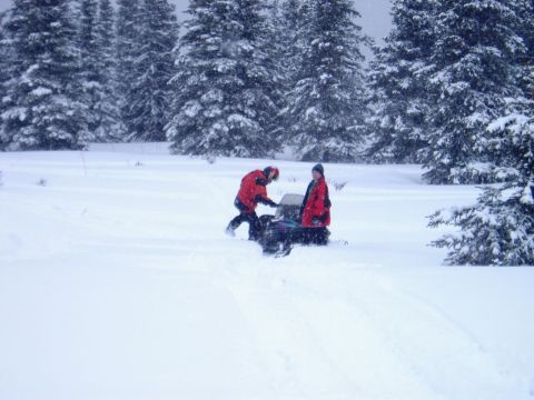 2000 Ford E350 - Two people are near a snowmobile in a snowy forest environment.