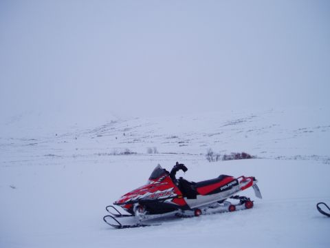 2000 Ford E350 - A red and white Polaris snowmobile sits idle in a wide, snow-covered landscape.