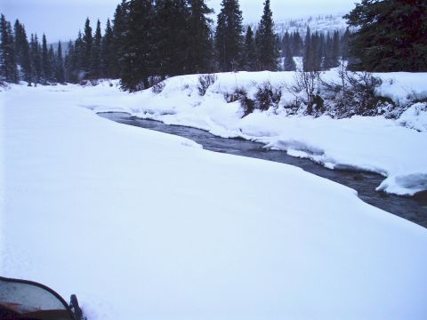 2000 Ford E350 - A winter scene with a partially frozen river surrounded by snow-covered banks and evergreen trees.