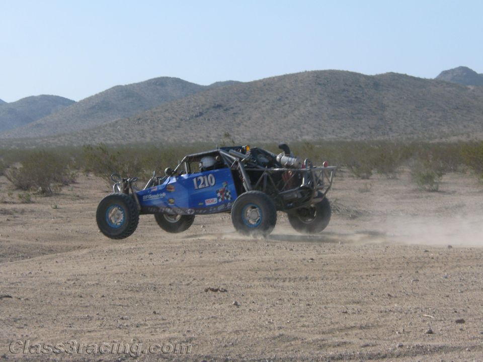 Blue tube-frame off-road buggy no. 1210 racing in the open desert