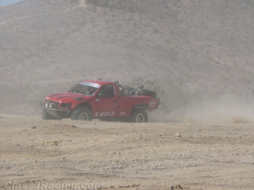 Red off-road race truck no. 1403 throwing dust on a desert course