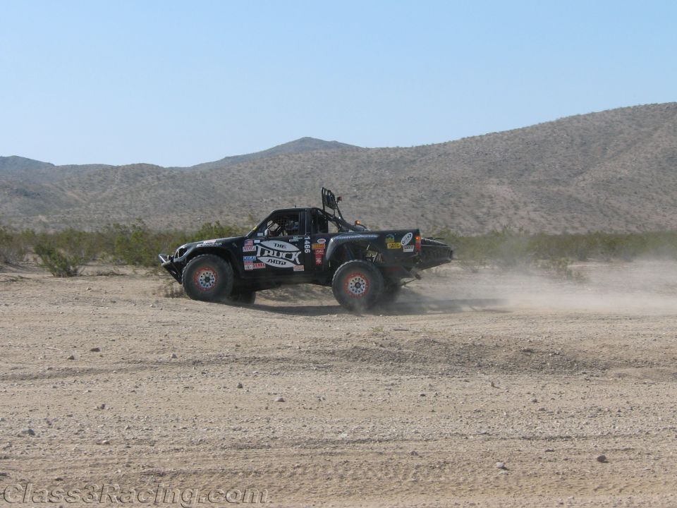 Black off-road race truck racing across open desert scrub